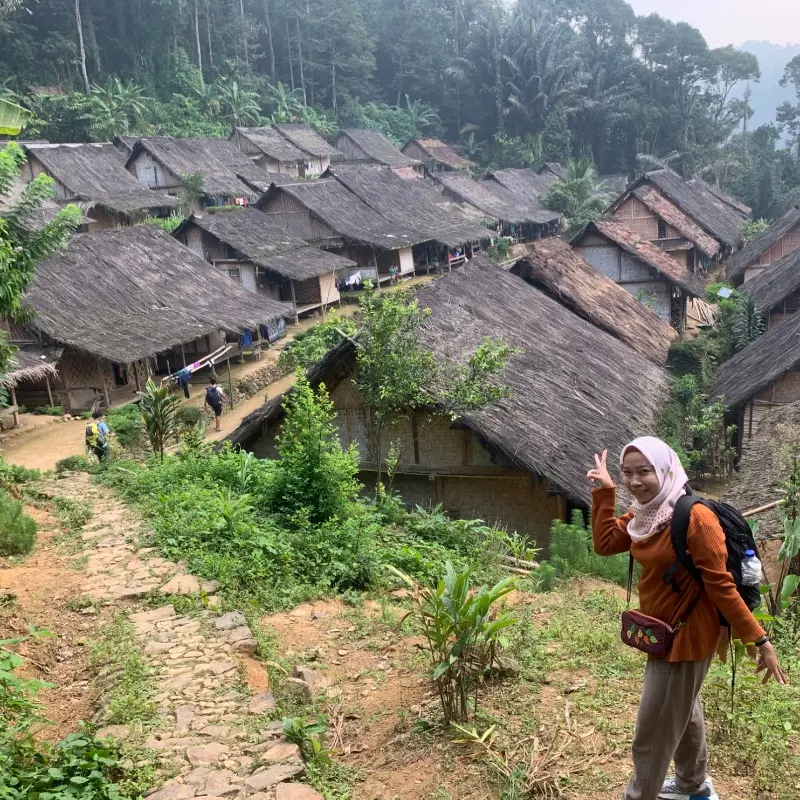 Peserta Open Trip Baduy berfoto dengan latar rumah adat Baduy Luar yang masih mempertahankan tradisi