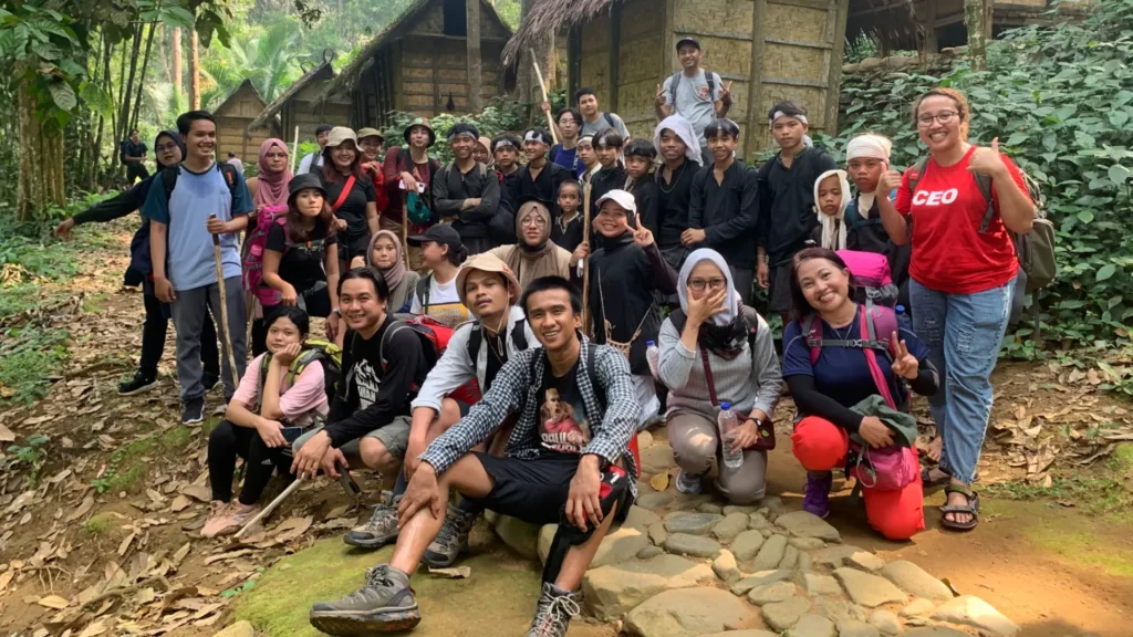 Peserta open trip Baduy sedang berfoto di depan rumah warga adat Baduy dalam suasana pedesaan yang asri